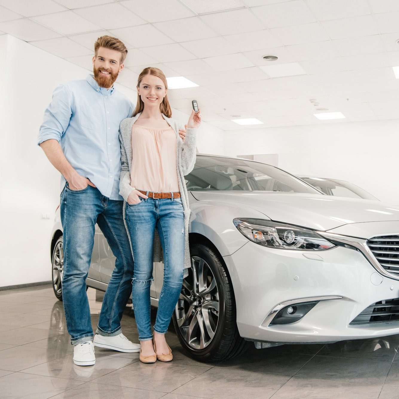 happy-couple-with-car-key-standing-at-car-in-dealership-salon